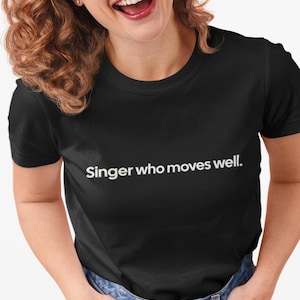 May include: Black t-shirt with the white text "Singer who moves well." The shirt is made of a soft material and has a classic crew neck design. The text is centered on the chest.