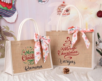May include: Two burlap tote bags with white handles and floral bows. One bag has "Merry Christmas Ramona" and the other says "Merry Christmas Vargas" in red script. The bags are decorated for Christmas.