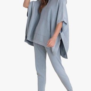 Könnte beinhalten: Ein hellblauer Kapuzenponcho mit einer Vordertasche und eine passende hellblaue Jogginghose. Das Outfit ist aus einem weichen Material gefertigt und auf Komfort ausgelegt. Das Model ist barfuß.
