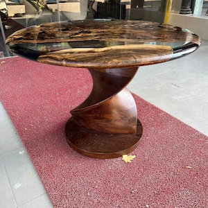 May include: A round table featuring a live edge wood slab tabletop with a dark resin inlay. The base is constructed from a single piece of solid wood carved into a continuous, spiraling, twisted shape that connects to a circular wooden floor base.