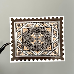 Pode incluir: Um autocolante com um design de mosaico semelhante a um selo postal. O design apresenta um padrão circular central rodeado por formas geométricas em tons de castanho, bege e branco. O autocolante tem uma borda castanha escura e o texto "@suheyart".