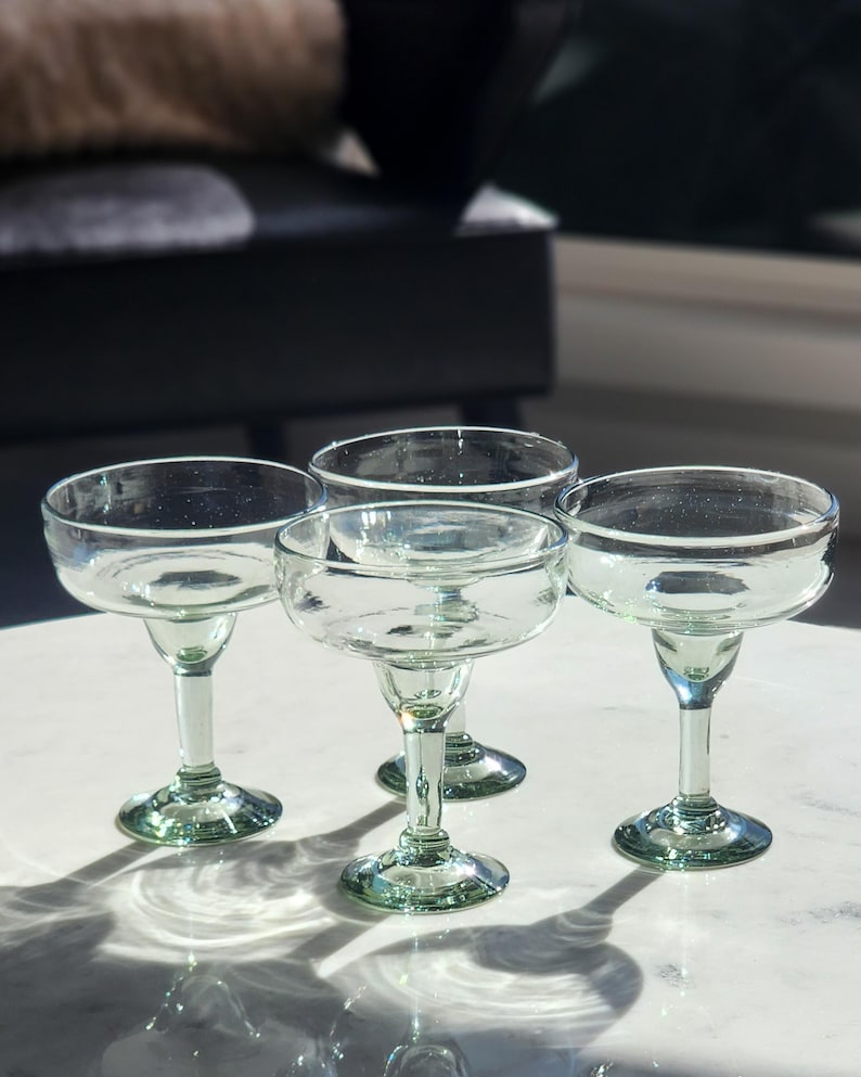 Pu&ograve; includere: Quattro bicchieri da margarita in vetro trasparente con bordi verdi. I bicchieri sono su una superficie bianca.