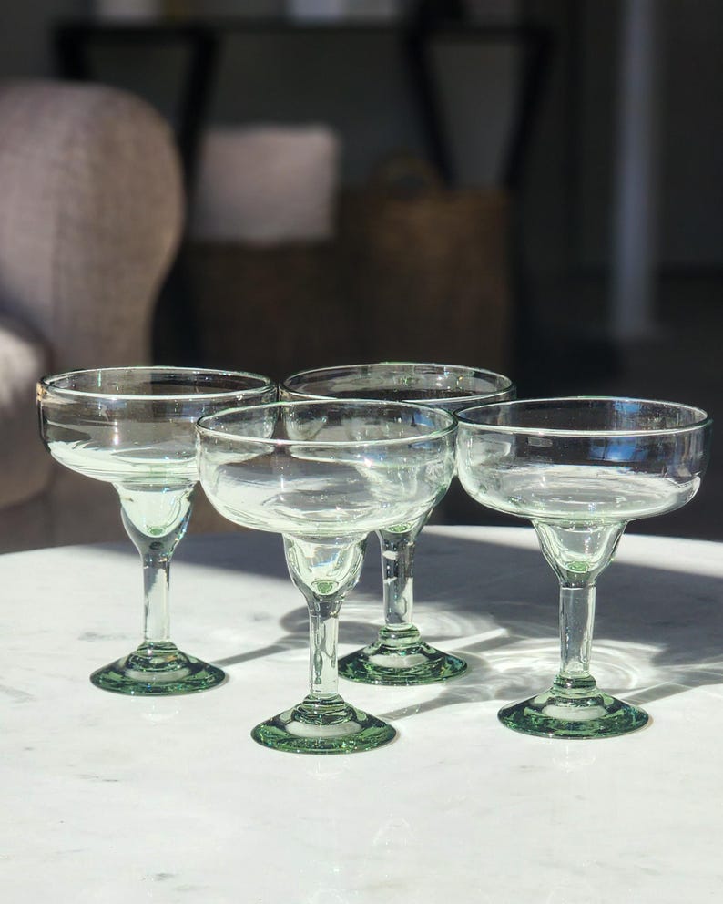 Pu&ograve; includere: Quattro bicchieri da margarita in vetro trasparente con bordi e basi verdi. I bicchieri sono disposti a semicerchio su una superficie bianca.