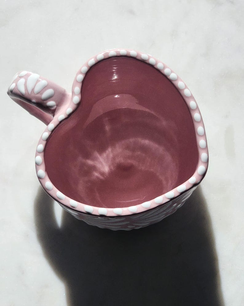 May include: A pink heart-shaped ceramic mug with a white polka dot design around the rim and handle.