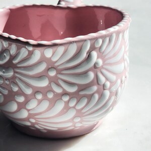 May include: A pink ceramic mug with a white floral design. The mug has a rounded shape and a handle.