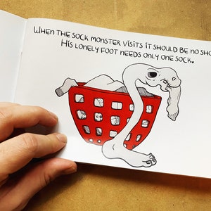 May include: A hand-drawn illustration of a sock monster with a single foot sticking out of a red laundry basket. The text reads "WHEN THE SOCK MONSTER VISITS IT SHOULD BE NO SHOCK: HIS LONELY FOOT NEEDS ONLY ONE SOCK."