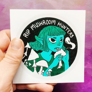 May include: A sticker with a green and blue cartoon character with elf ears eating a mushroom. The character is surrounded by mushrooms and the text "RIP MUSHROOM HUNTERS" is in a circle around the character.