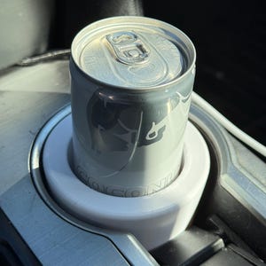 May include: A silver can of Red Bull Coconut Edition in a white cup holder in a car.