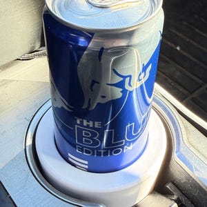 May include: A blue and silver can of Red Bull The Blue Edition in a white cup holder.