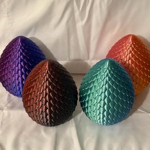 May include: Four dragon egg-shaped decorative objects with a scaly texture. The eggs are purple, brown, teal, and orange.