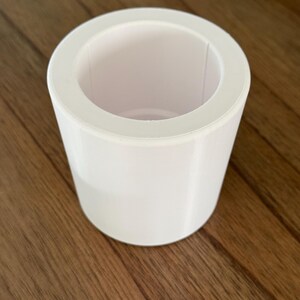 May include: A white cylindrical planter with a smooth, matte finish. The planter has a wide opening at the top and a slightly smaller base.