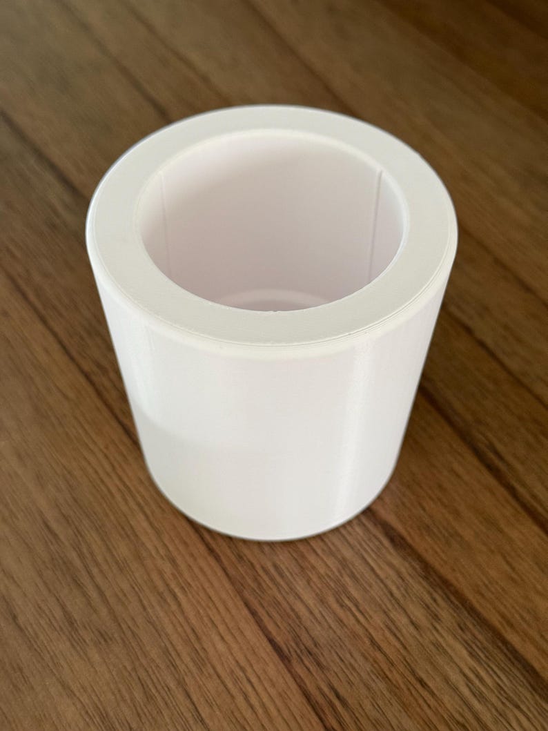 May include: A white cylindrical planter with a smooth, matte finish. The planter has a wide opening at the top and a slightly smaller base.