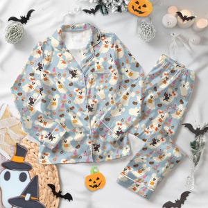 Peut inclure: Ensemble de pyjama d'Halloween bleu clair avec un motif répété de fantômes, de chats et de citrouilles. Le haut à manches longues et le pantalon ont une bordure blanche. Le pyjama est en matière douce et confortable.