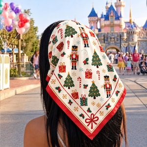 Puede incluir: Un pañuelo cuadrado con fondo crema y un patrón festivo de cascanueces, árboles de Navidad, regalos envueltos, bastones de caramelo y hojas de acebo, terminado con un borde rojo sólido y un gráfico de lazo rojo en la punta inferior.