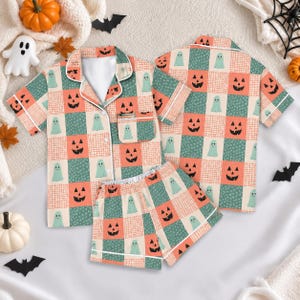 May include: A short-sleeve button-down pajama shirt and matching shorts set featuring a checkered pattern of orange jack-o'-lantern faces on a grid background and light teal ghosts on a dark teal floral background with white piping trim.
