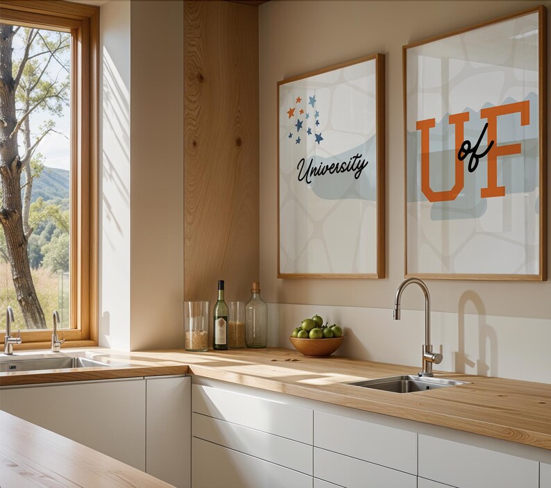 May include: A modern kitchen with white cabinets and a wooden countertop. There is a sink with a chrome faucet and a window with a view of trees. Two framed prints on the wall say "University of" and "University".