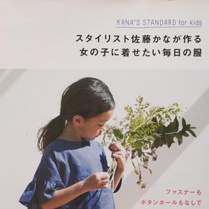 以下が含まれることがあります： 青いシャツとカーキ色のズボンを着た若い女の子が花束を持っている本の表紙。本のタイトルは「KANA'S STANDARD for kids」で、副題は「スタイリスト佐藤かなが作る 女の子に着せたい毎日の服」。本の表紙には、「ファスナーも ボタンホールもなしで 簡単かわいい」と「一年中使える コーディネート実例 55」のテキストも含まれています。