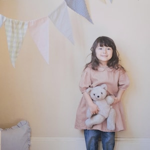 以下が含まれることがあります： ピンクと白のカラーリングで、女の子がテディベアを抱っこしている表紙の書籍。書籍のタイトルは「a sunny spot 女の子のまいにちの服」で、「a sunny spot 女の子のまいにちの服」は「a sunny spot 女の子のまいにちの服」と訳されます。書籍の作者は村田 繭子で、「村田 繭子」は「Mayuko Murata」と訳されます。
