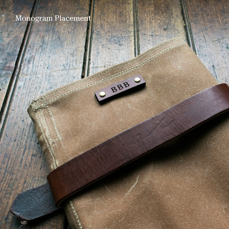 May include: A brown canvas bag with a brown leather strap and a brass monogram plate that reads "BBB".