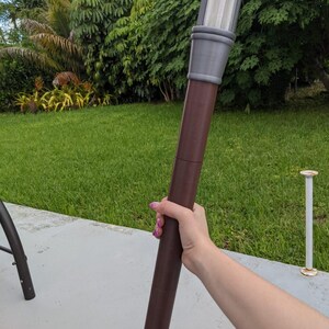 May include: A brown and gray torch with a white light source at the top. The torch is held in a person's hand.