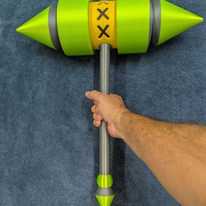 May include: A large, stylized hammer with a neon green head and accents, a yellow center with black cross-shaped details, and a gray handle. The hammer is held against a blue background.