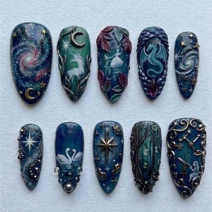 May include: A set of ten intricately designed artificial nails. Each nail features a unique, hand-painted design with celestial and fantasy themes, including galaxies, dragons, and constellations. The color palette includes blues, greens, and metallic accents.