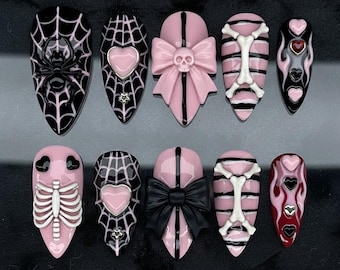 May include: A set of ten press-on nails with a gothic theme. Designs include spiderwebs, spiders, hearts, bows with skulls, and rib cages. The nails are primarily black and pink, with white and red accents.