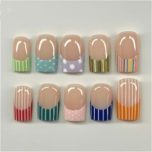 May include: A collection of ten false nails, each with a French manicure style. The nails have a nude base with a white tip and a patterned design at the base, featuring stripes and polka dots in various colours.