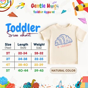May include: A cream-colored toddler t-shirt with a blue and red croissant graphic and the text "le croissant". The shirt is displayed with a size chart showing length in inches and weight in pounds.