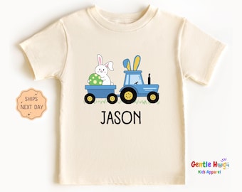 May include: A light cream colored t-shirt with a blue tractor pulling a wagon with a white bunny holding a green Easter egg. The text "JASON" is printed below the tractor.