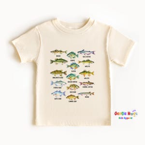May include: Cream-colored t-shirt featuring a colorful illustration of various fish species, each labeled with its name. The design includes fish like bass, crappie, and catfish. The text "Gentle Hug Kids Apparel" is in the lower right corner.
