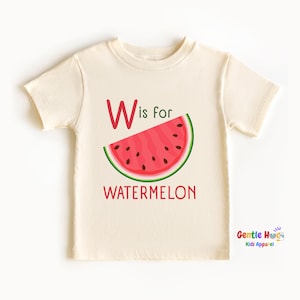 May include: Cream-colored toddler t-shirt featuring a watermelon slice graphic. The design includes the text "W is for WATERMELON" in red. The shirt is short-sleeved and has a round neckline. The brand logo "Gentle Hugs Kids Apparel" is in the bottom right corner.