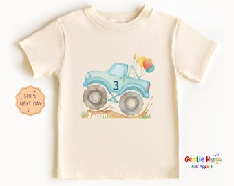May include: Cream-colored toddler t-shirt featuring a light blue monster truck graphic with the number 3, balloons, and the name "Jason." The truck has large wheels and is set against a watercolor-style background. The shirt is made of soft material.