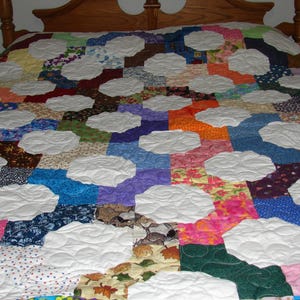 May include: A white quilt with a patchwork design featuring various colors and patterns. The quilt is made up of many small squares and rectangles, each with a different fabric. The quilt is quilted with a white thread, creating a raised design.
