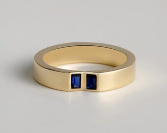 May include: A gold-colored ring with a flat band and two square, dark blue gemstones set side-by-side. The ring has a simple, modern design, and the gemstones provide a contrasting pop of color.