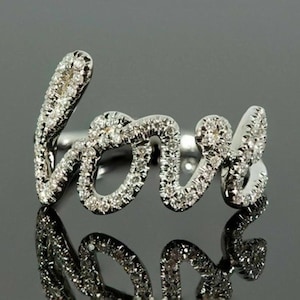 May include: A silver ring spelling out the word "love" in cursive script. The ring is encrusted with small, sparkling diamonds, creating a brilliant display. The ring's design is elegant and romantic, perfect for a special occasion.
