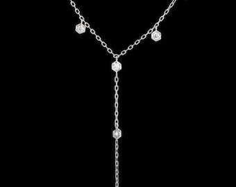 May include: A delicate silver necklace with a Y-shaped design. The necklace features multiple hexagonal-shaped clear gemstones, with a longer strand of gemstones hanging down. The background is solid black.