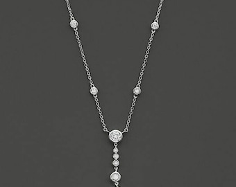 May include: A delicate silver necklace featuring a series of round, sparkling gemstones. The necklace has a simple chain with evenly spaced gems, and a longer strand of descending gems. The necklace is displayed against a dark gray background.