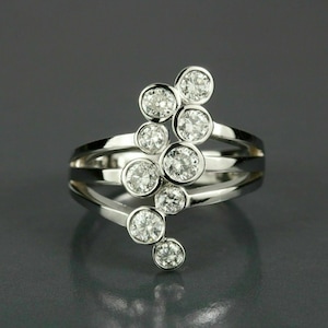 May include: A silver ring with multiple clear, round gemstones. The ring features a unique design with a cluster of stones set in individual bezels, creating a sparkling, eye-catching effect. The band has a layered design.