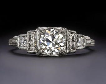May include: A vintage engagement ring with a large, round, brilliant-cut diamond set in a platinum band. The band is decorated with smaller diamonds on either side of the center stone.