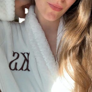 May include: White bathrobe with a fluffy collar and embroidered initials "2X" on the left side.