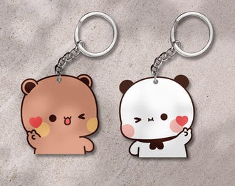 May include: Two cartoon bear keychains. One is brown with a red heart and the other is white with a black bow tie and a red heart. Both have silver key rings and chains.