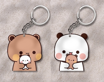 May include: Two keychains with cartoon bear designs. One is brown with a white bear, the other is white with a brown bear. Each keychain has a silver chain and ring. The bears are holding smaller bears.