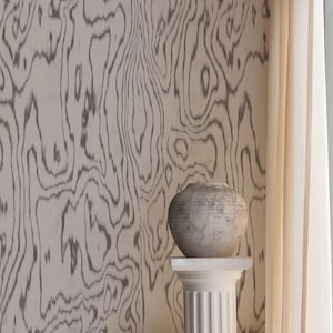 Könnte beinhalten: Eine graue, strukturierte Keramikvase steht auf einem weißen, geriffelten Sockel. Der Hintergrund zeigt eine Wand mit einem grauen Holzmaserungsmuster. Ein cremefarbener Vorhang ist sichtbar. Die Szene strahlt rustikale Eleganz aus.