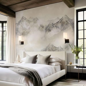 May include: A modern bedroom with a white bed, gray pillows, and a gray throw blanket. The headboard is white, and the wall behind the bed features a mountain mural. Two sconces are mounted on the wall. A side table with a vase of flowers sits next to a large window.