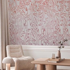 May include: A room with a light-colored, textured wall with a red and white wood grain pattern. A beige, fluffy armchair sits near a wooden coffee table. A small, mushroom-shaped lamp and a vase with cotton stems are also visible.