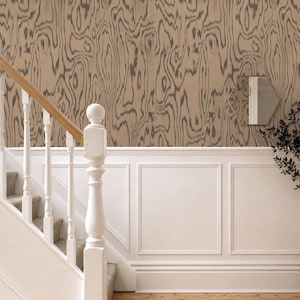 May include: Wallpaper featuring a tan and dark gray wood grain pattern applied to a wall above white wainscoting. The wall is positioned next to a white staircase with a wooden handrail and a small hexagonal mirror hanging on the wall surface.