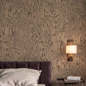May include: A bedroom interior featuring wallpaper with a brown and dark gray wood grain pattern, a dark purple upholstered headboard, a light beige pillow, a dark wood nightstand, and a wall-mounted lamp with a white cylindrical shade.