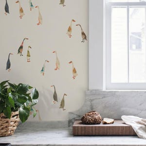 May include: A wall covered in off-white wallpaper featuring a repeating pattern of watercolor-style geese in various shades of brown, gray, green, and orange. The geese are depicted in different poses and sizes, scattered across the light surface.