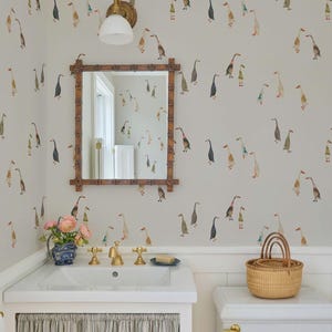 a bathroom with a white sink, a mirror, a toilet, and a basket on the toilet tank. The walls are decorated with a pattern of ducks and geese, and there is a vase of flowers on the sink.